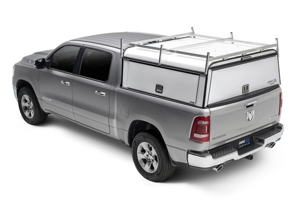 White A.R.E. DCU Series aluminum work cap with a roof rack on a silver Ram pickup, rear three-quarter view