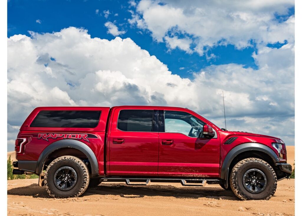 A.R.E. CX Revo truck cap on a red pickup parked on sand under a blue sky