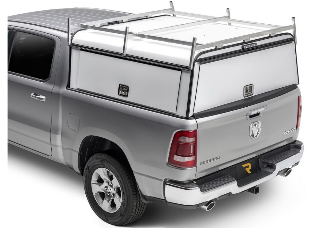 White A.R.E. DCU Max aluminum work cap with a roof rack on a silver Ram pickup, rear view