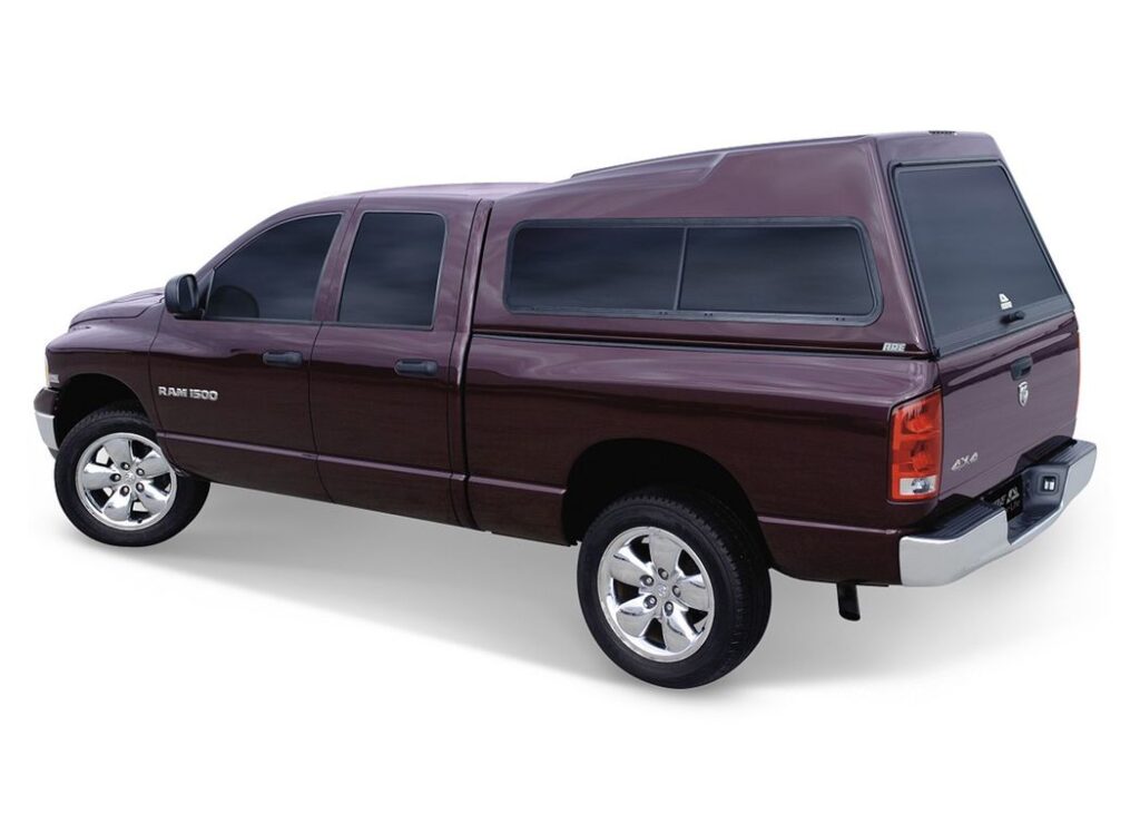 Side view of a maroon, paint-matched A.R.E. TW Series wedge-roof truck cap on a maroon Ram 1500